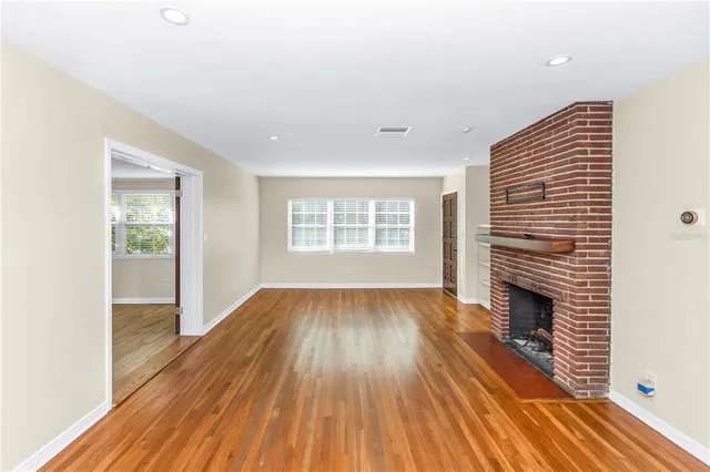 a view of an empty room with wooden floor fireplace and a window