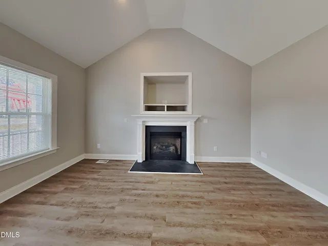 a view of an empty room with wooden floor fireplace and a window