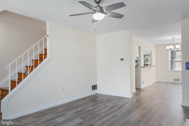 a view of an empty room with wooden floor and a ceiling fan