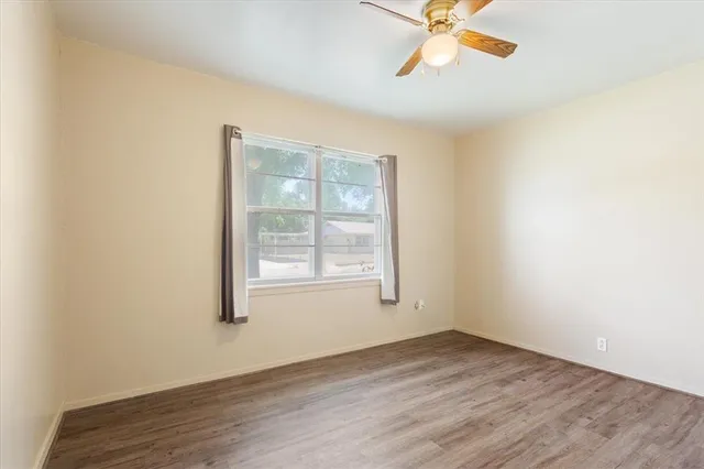 an empty room with wooden floor fan and windows