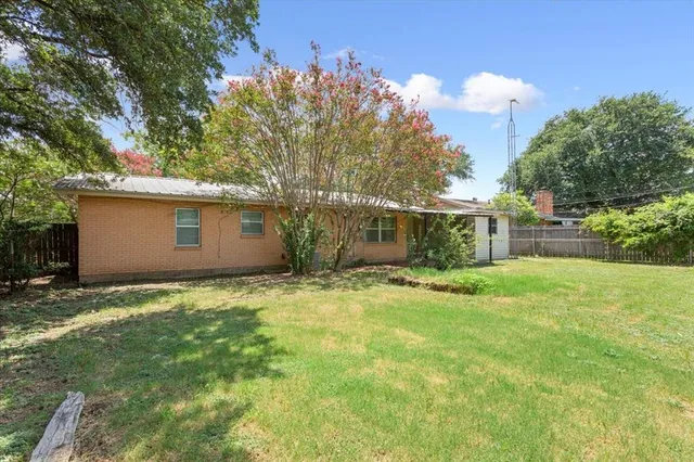 a backyard of a house with table and chairs plants and large tree