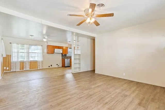 an empty room with wooden floor chandelier fan and windows