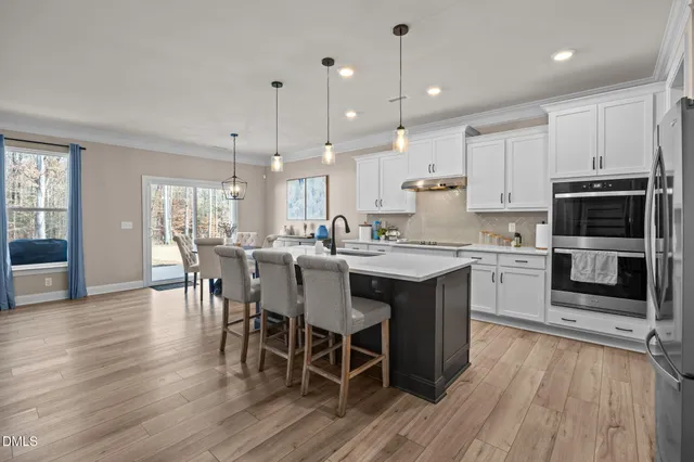 a kitchen with a dining table chairs wooden floor cabinets and appliances