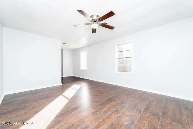 a view of an empty room with wooden floor and a ceiling fan