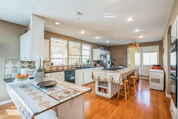 a kitchen with stainless steel appliances granite countertop a stove top oven a sink dishwasher and a dining table with wooden floor