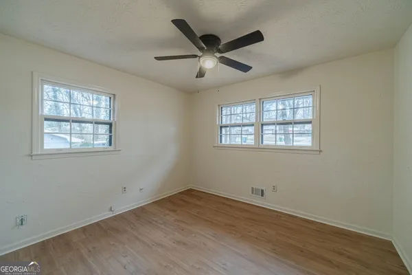 an empty room with wooden floor ceiling fan and windows