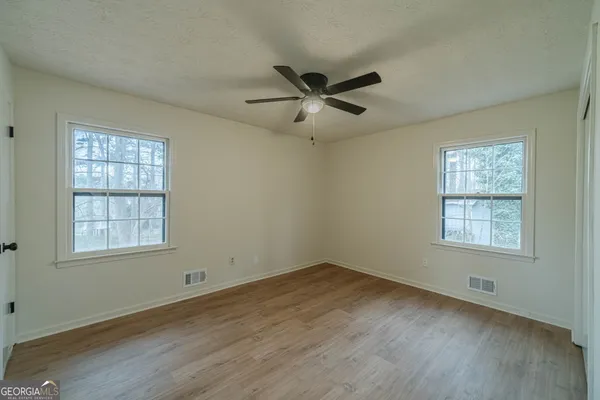 an empty room with wooden floor ceiling fan and windows