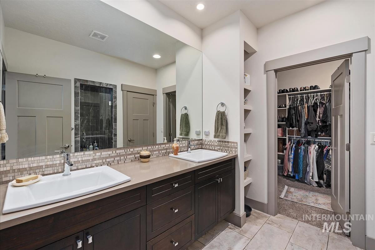 24398 Tombstone Ridge Court Middleton, ID 83644 - Photo 20 of 48 Dual vanity with integrated sinks, mosaic tile backsplash, dark wood-finish cabinetry, and built-in shelving