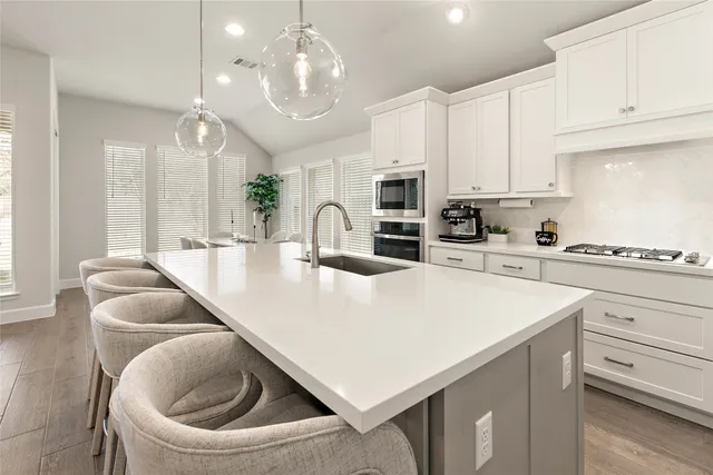 a kitchen with stainless steel appliances a stove a sink a microwave a refrigerator and white cabinets with wooden floor