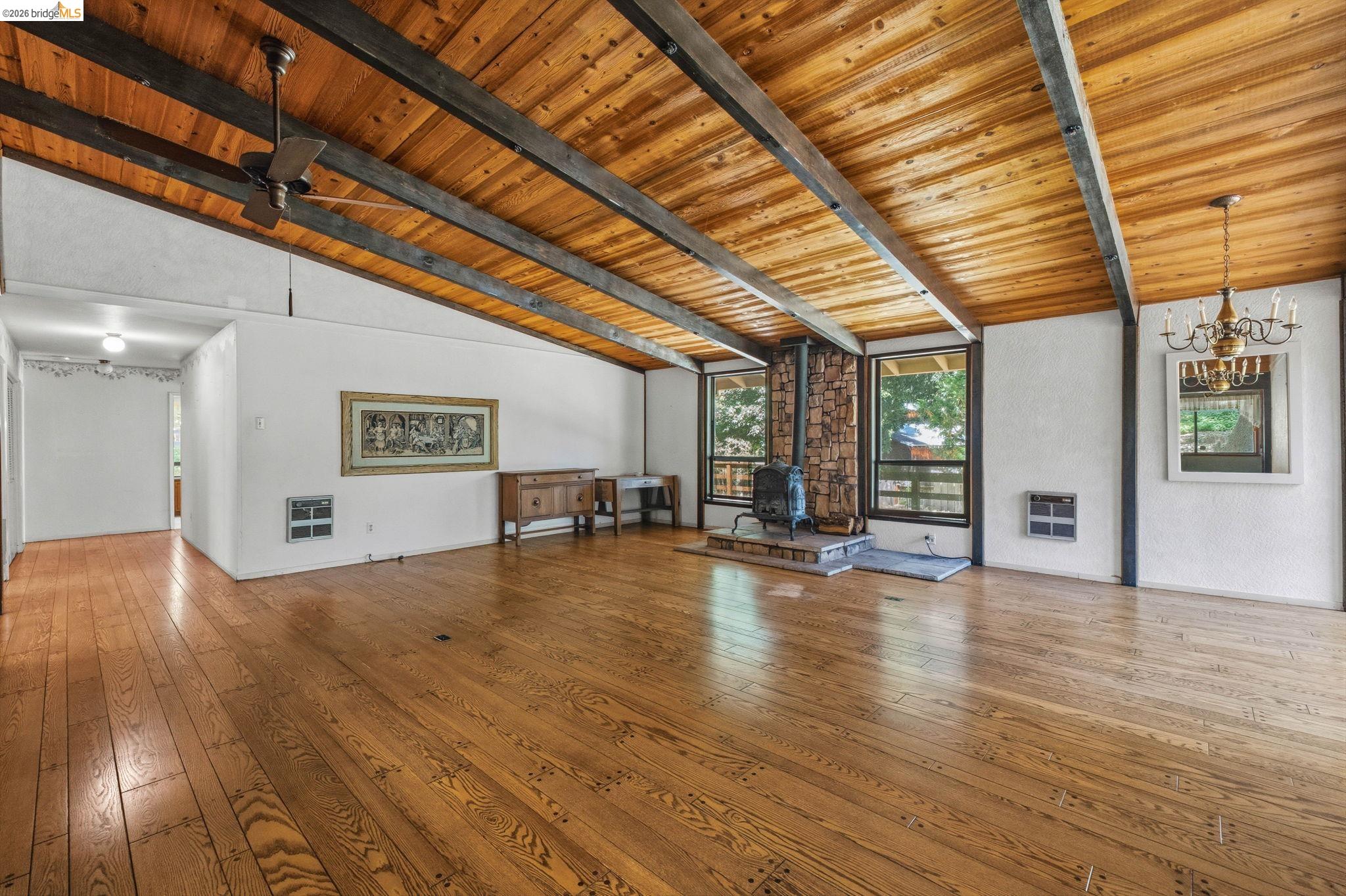 22401 South Fork Road Sonora, CA 95370 - Photo 15 of 34 Spacious room featuring wood-finish flooring, an exposed beam wood ceiling, a stone-clad fireplace with a stove insert, multiple large windows, and a chandelier