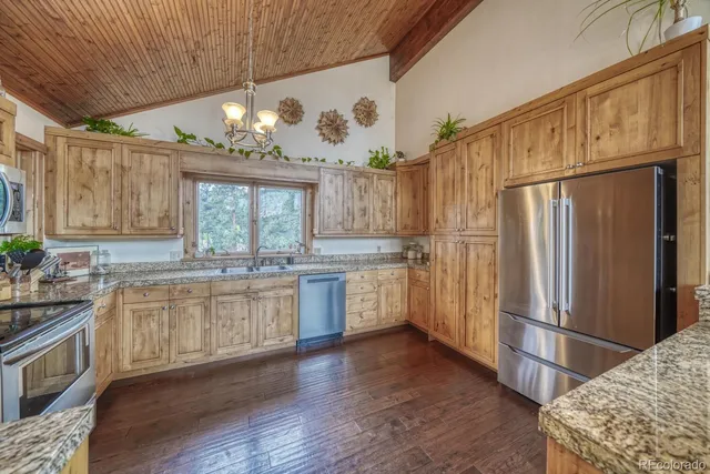 a kitchen with granite countertop a refrigerator a sink dishwasher a stove and white cabinets with wooden floor