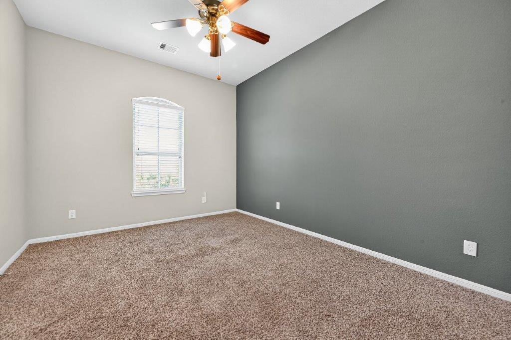 5710 Metaphor Way Richmond, TX 77469 - Photo 30 of 41 Another bedroom is accented by a tall window and a muted gray wall, creating a modern, restful palette.