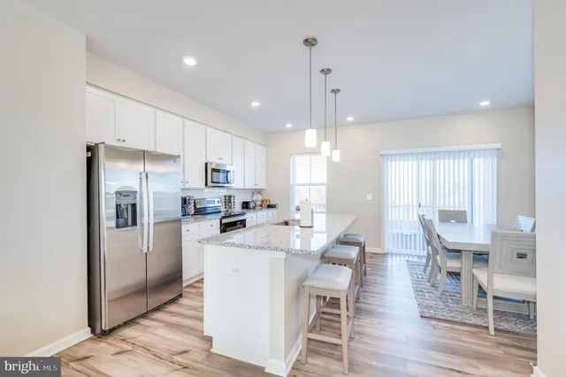 a kitchen with stainless steel appliances granite countertop a refrigerator a sink a stove a dining table and chairs