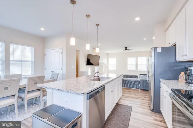 a kitchen with stainless steel appliances kitchen island granite countertop a sink dishwasher a microwave oven a stove with white cabinets and wooden floor