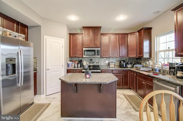 a kitchen with stainless steel appliances granite countertop a refrigerator a sink dishwasher a stove and a dining table with wooden cabinet