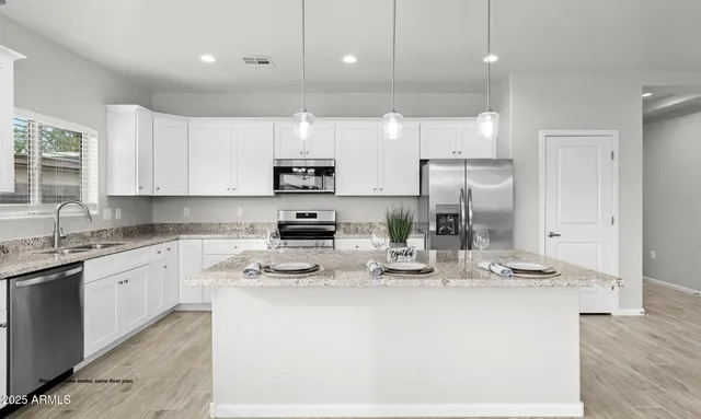 a kitchen with kitchen island granite countertop a stove a sink a refrigerator and white cabinets with wooden floor