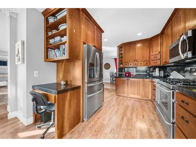 a kitchen with stainless steel appliances granite countertop a refrigerator a stove and a sink with wooden cabinets