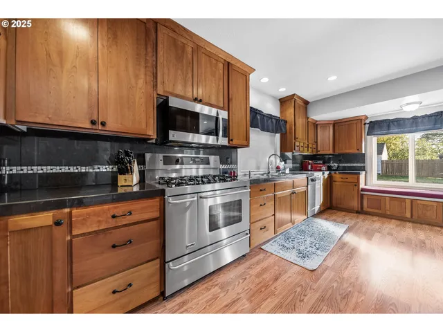 a kitchen with stainless steel appliances granite countertop a stove a sink dishwasher and a microwave oven with wooden cabinets