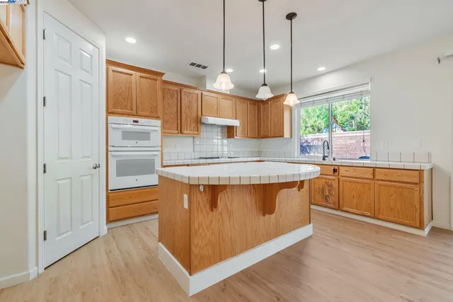 a kitchen with stainless steel appliances granite countertop a sink a stove a refrigerator cabinets and wooden floor