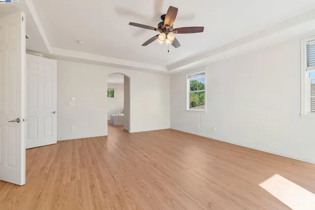 an empty room with wooden floor chandelier fan and windows