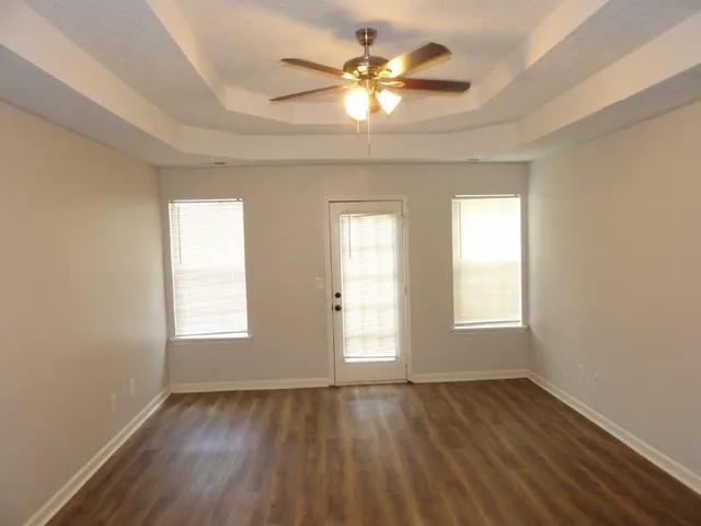 an empty room with wooden floor chandelier fan and windows