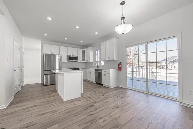 a kitchen with stainless steel appliances granite countertop a refrigerator a sink dishwasher a stove and white countertops with wooden floor