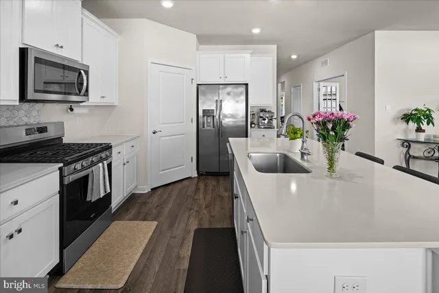 a kitchen with stainless steel appliances a microwave a stove a sink a refrigerator white cabinets a dining table and chairs