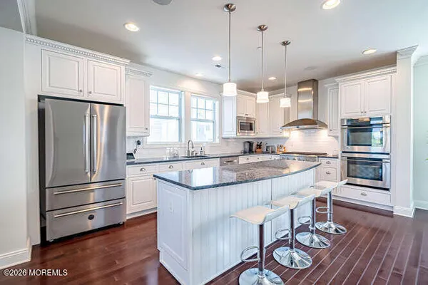 a kitchen with granite countertop a refrigerator a stove a sink and white cabinets with wooden floor