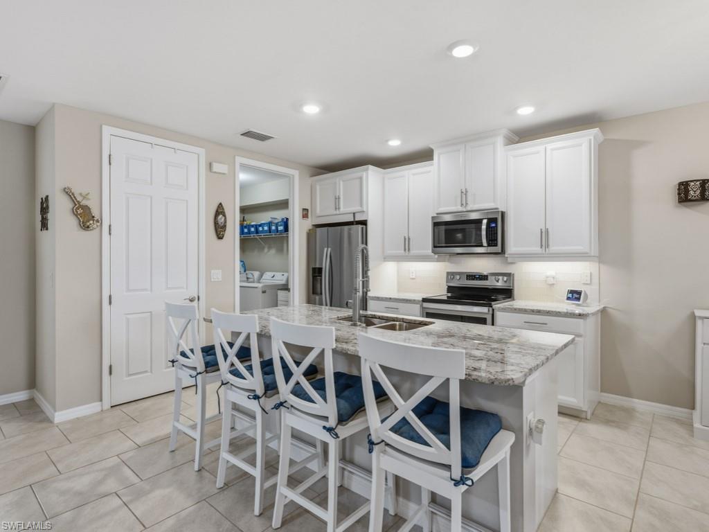 14591 Edgewater Circle Naples, FL 34114 - Photo 2 of 36 Kitchen with white cabinetry, a breakfast bar area, stainless steel appliances, granite countertops, pantry and a kitchen island with sink