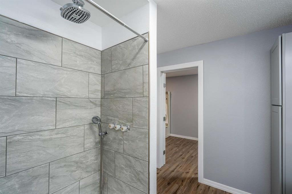 365 Co Road Stamford, TX 79553 - Photo 14 of 23 Shower with large format gray tile and rainfall showerhead, complemented by light gray walls and wood-finish flooring