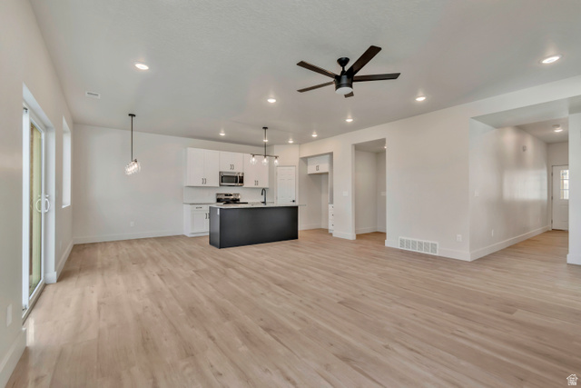 2535 West Santa Fe Drive Mapleton, UT 84664 - Photo 26 of 26 Two tone kitchen with open floor plan, light wood-style flooring, a ceiling fan, decorative light fixtures, and a center island with sink