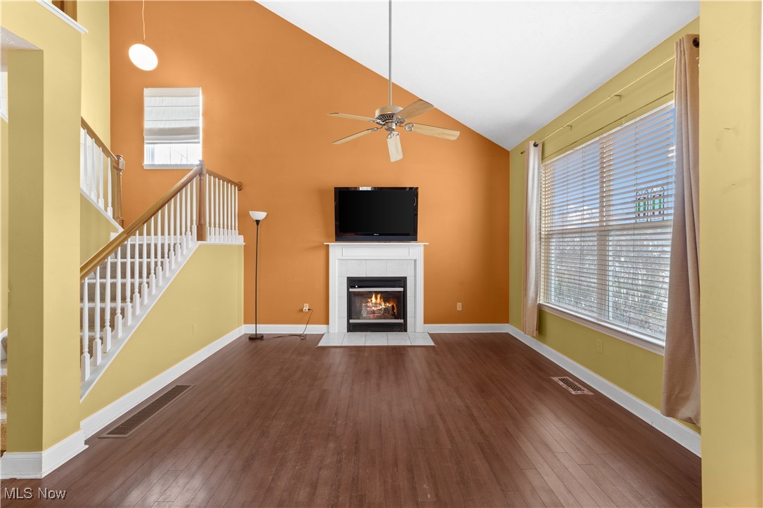 Unfurnished living room featuring a wealth of natural light, a fireplace, ceiling fan, and dark wood-type flooring