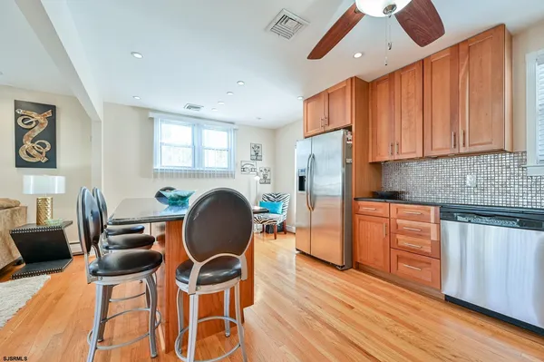 a kitchen with stainless steel appliances granite countertop a stove top oven a refrigerator a dining table and chairs with wooden floor