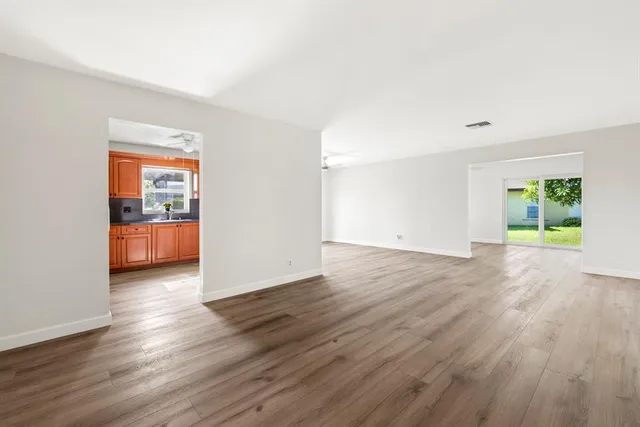 an empty room with wooden floor and way to kitchen