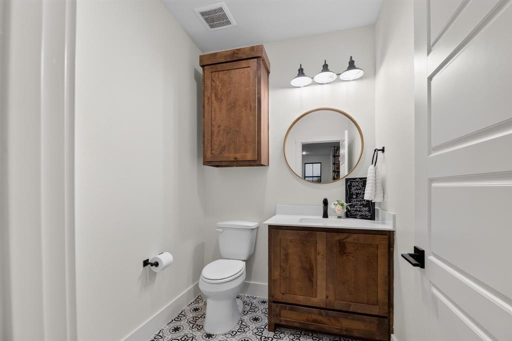 985 Vest Lane Pilot Point, TX 76258 - Photo 35 of 40 Bathroom featuring patterned floor tiling, a wood-finish vanity with a white countertop, a circular gold-framed mirror, and a three-light vanity fixture
