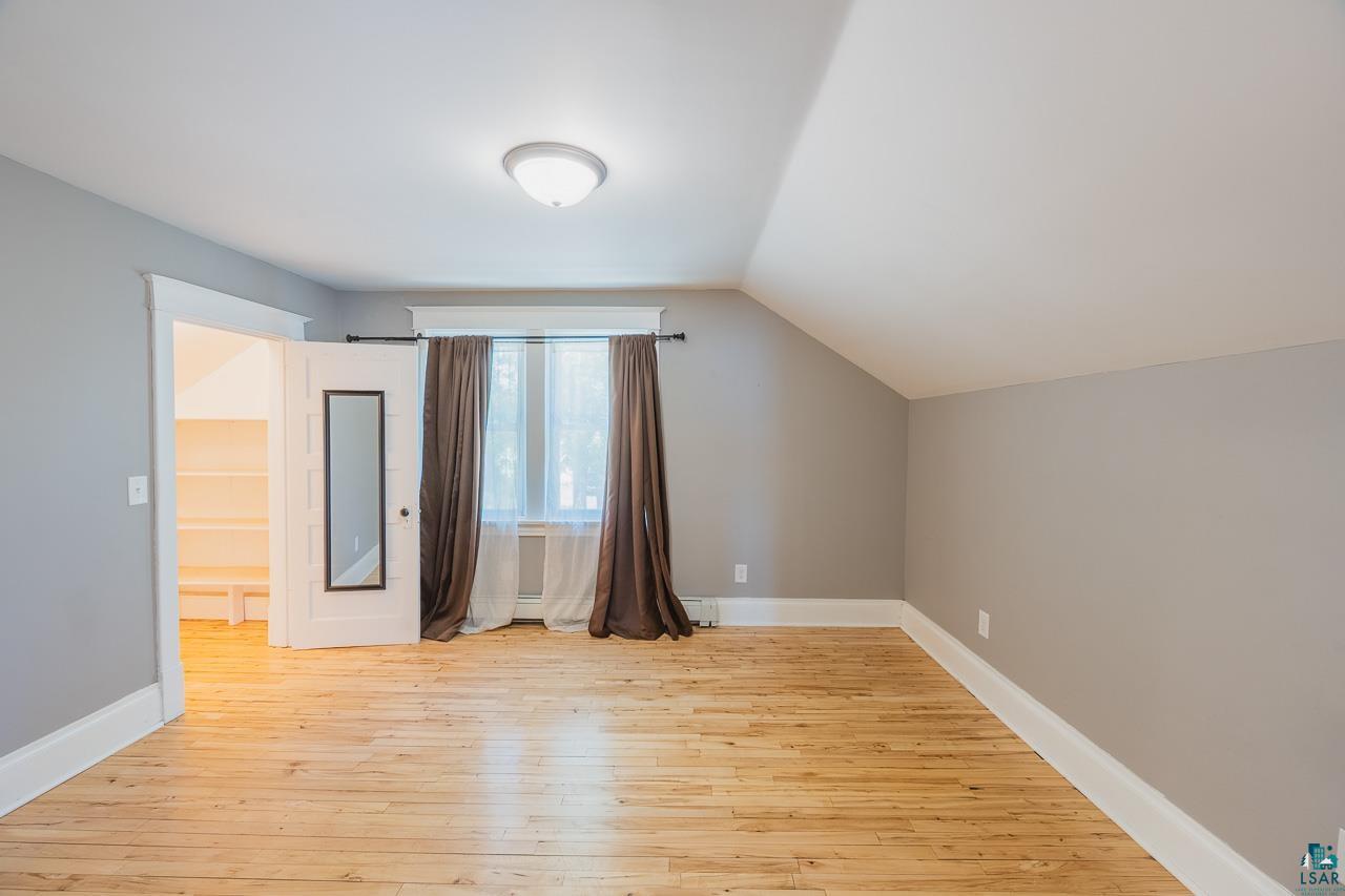 508 10th Street South Virginia, MN 55792 - Photo 18 of 43 Hardwood flooring spans this room featuring light gray walls, white trim, and a sloped ceiling