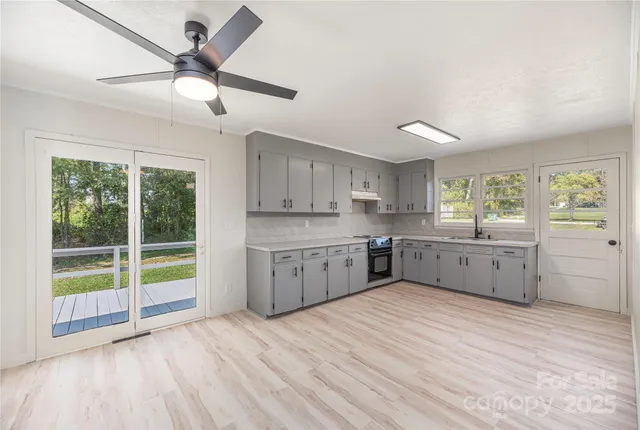 a kitchen with stainless steel appliances granite countertop a stove a sink dishwasher and white cabinets with wooden floor