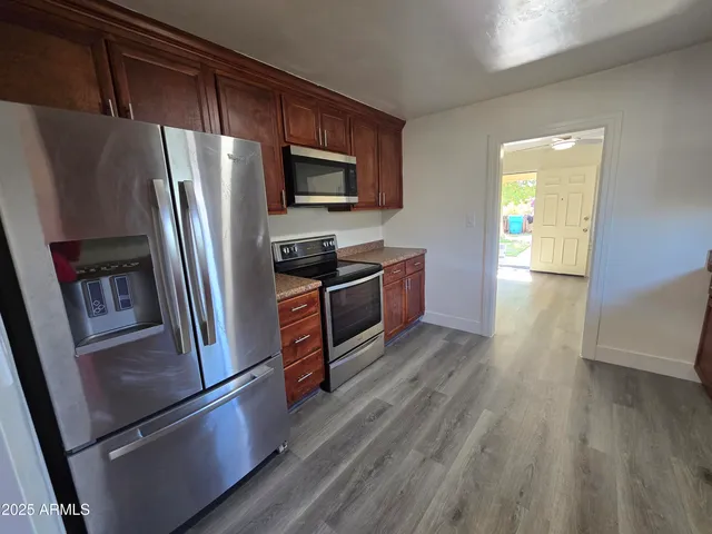 a kitchen with stainless steel appliances granite countertop a refrigerator a sink dishwasher a stove and white countertops with wooden floor