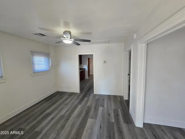 a view of an empty room with wooden floor and a ceiling fan