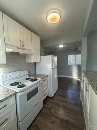 a kitchen with granite countertop a stove a sink dishwasher and white cabinets with wooden floor