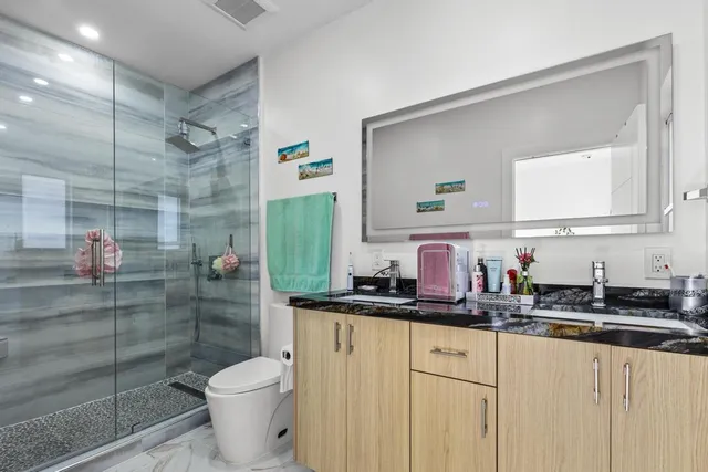 a bathroom with a granite countertop sink a toilet a mirror and shower