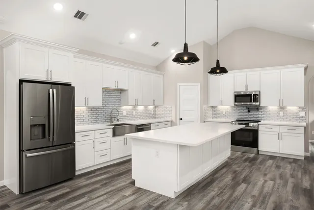 a large kitchen with stainless steel appliances kitchen island a refrigerator sink and white cabinets