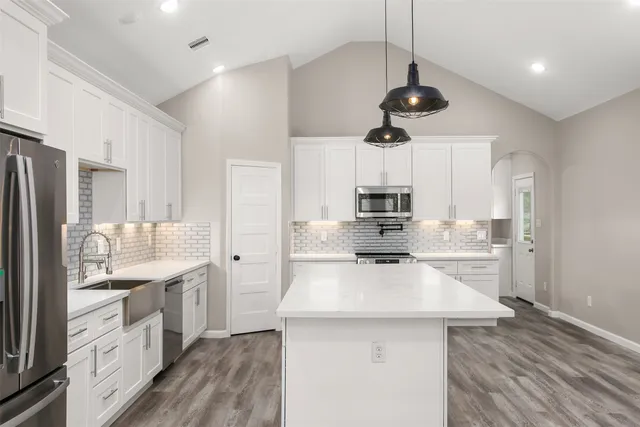 a kitchen with stainless steel appliances a sink a stove a refrigerator cabinets and wooden floor