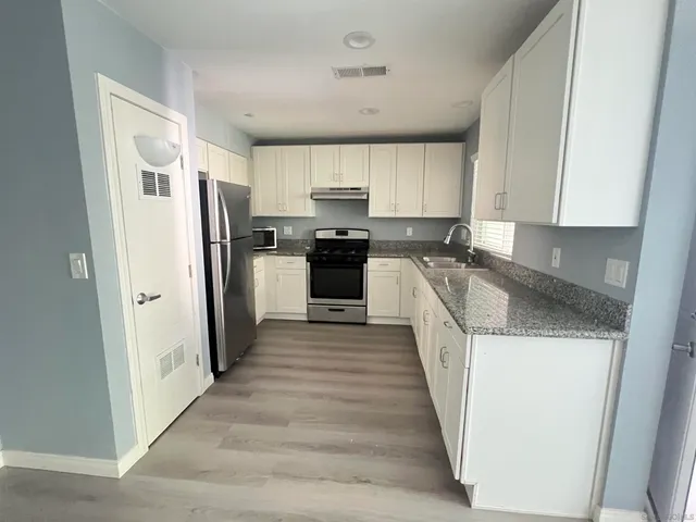 a kitchen with stainless steel appliances a refrigerator a sink a stove oven and white cabinets