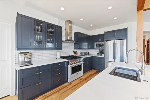 a kitchen with stainless steel appliances granite countertop a refrigerator a sink dishwasher a stove and white countertops with wooden floor