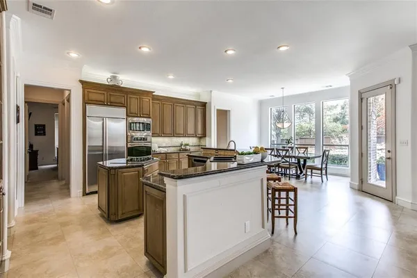 a kitchen with stainless steel appliances granite countertop a stove top oven a refrigerator a sink a dining table and chairs with wooden floor