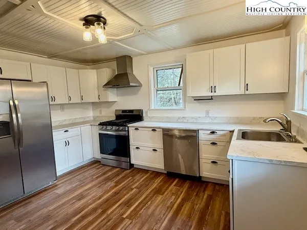 a kitchen with stainless steel appliances a stove a sink dishwasher a refrigerator and white cabinets with wooden floor
