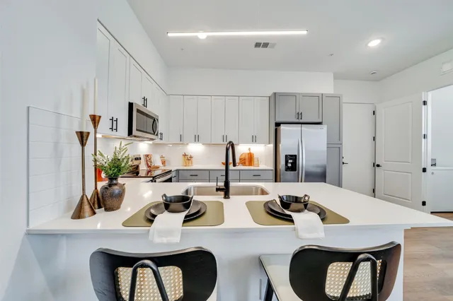 a kitchen with stainless steel appliances kitchen island granite countertop a dining table chairs refrigerator and sink