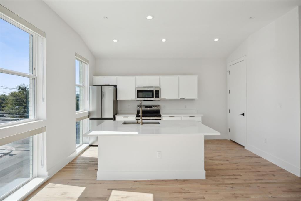 4907 Bryan Street Dallas, TX 75204 - Photo 17 of 21 a large white kitchen with wooden floor and stainless steel appliances