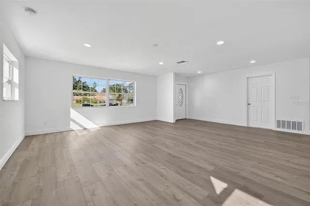 a view of an empty room with wooden floor and a window